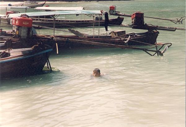 Child swimming in turquoise water among Thai longtail boats