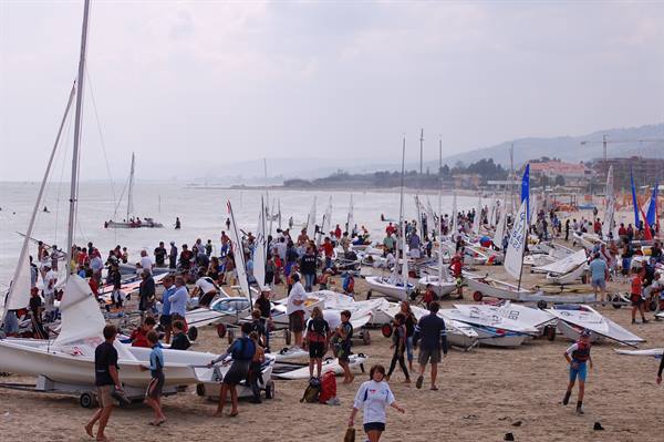 Crowded beach with sailboats and people preparing for a regatta