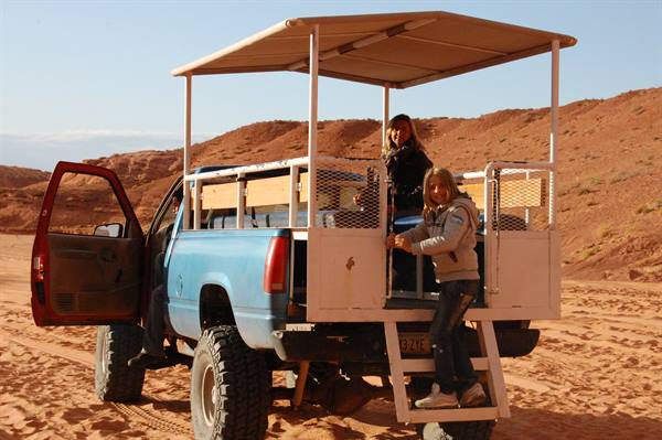 Tourists climb down a blue canopy truck among red sand dunes at Antelope Canyon