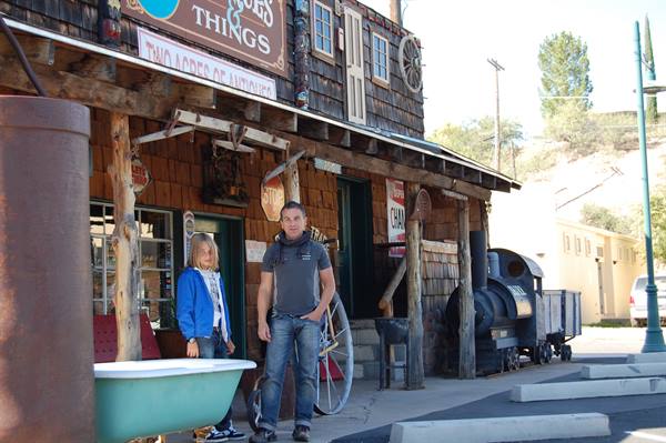 Man and girl in front of a wooden antiques shop, with vintage locomotive