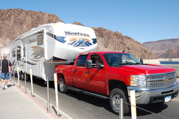 Red pickup truck towing a Montana RV near brown cliffs, Hoover Dam