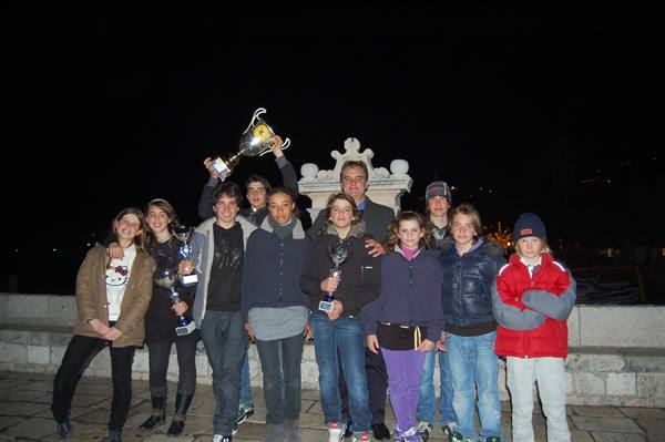 Group of young people with trophies at night beside a stone monument