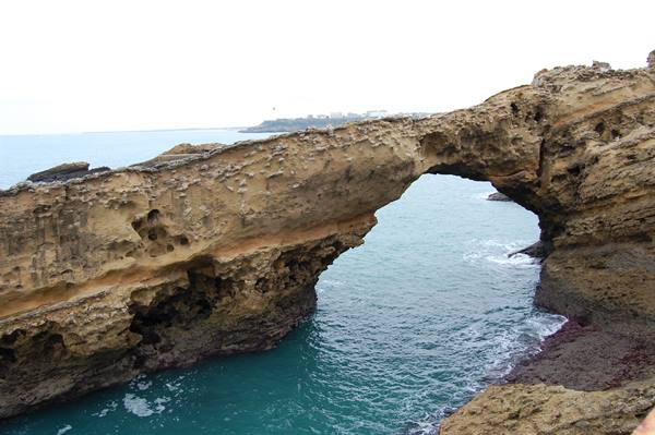 Natural limestone arch over turquoise water, waves foaming below