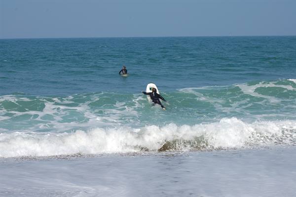 Wetsuit surfer paddles over the wave through white foam, another waits offshore