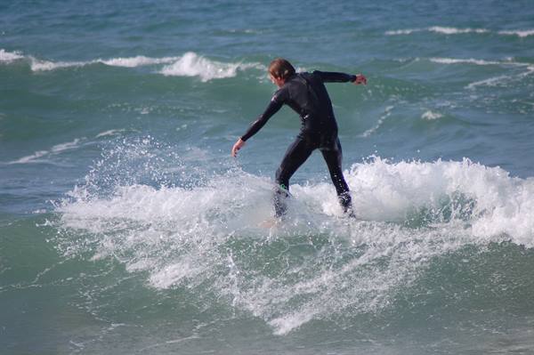 Surfer in black wetsuit balancing on the foamy wave