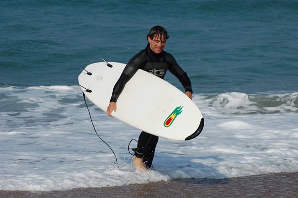 Surfer in black wetsuit walks out of the waves carrying a white surfboard