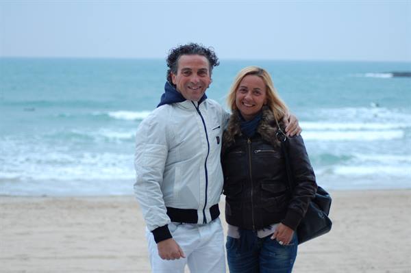 Smiling couple embracing on the beach, winter jackets, waves and grey sky behind