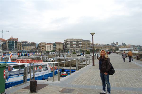 Smiling woman on Santander harbor promenade, boats and city buildings behind