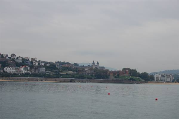 San Sebastián bay: grey sea with buoys, houses and cathedral towers under overcast sky
