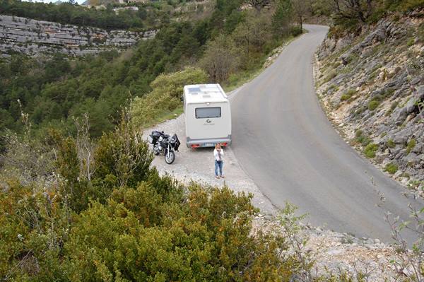 Motorhome and motorcycle parked on an asphalt road among shrubs and rocky cliffs