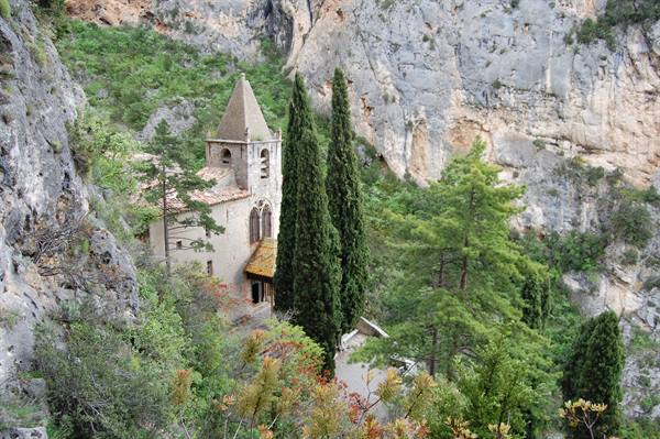 Small chapel with bell tower nestled against cliffs among cypresses and pines