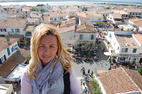 Smiling woman with scarf above tiled roofs and busy square in Saintes-Maries-de-la-Mer