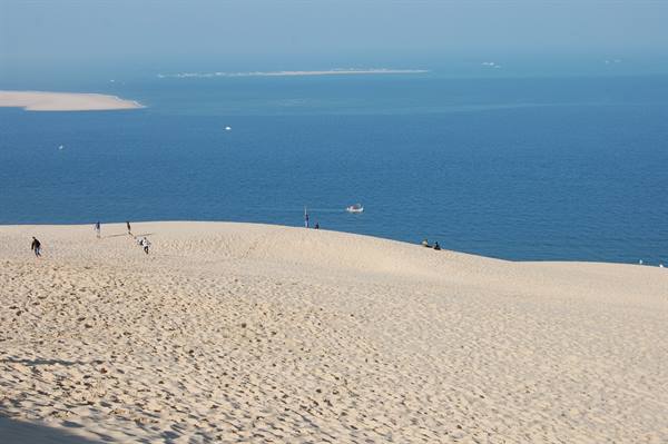 Visitors walk on the sandy Dune du Pilat facing the blue ocean