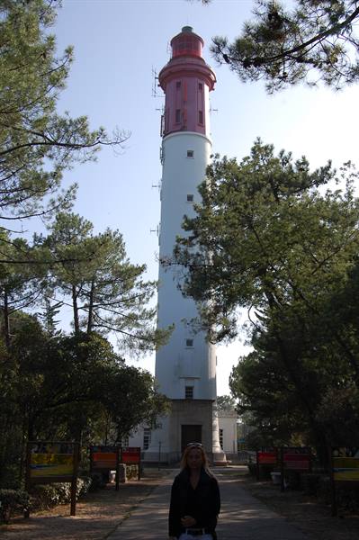 Woman in front of the red and white Cap-Ferret lighthouse among pines