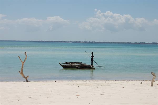 Fisherman standing on wooden boat in turquoise water, white sand beach