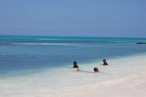 Three children swim in the turquoise water near the white sand