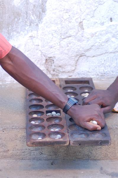Two hands playing awalé, sowing seeds across a carved wooden board