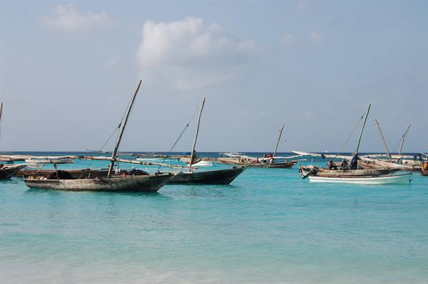 Wooden sailboats anchored in clear turquoise water under a partly cloudy sky