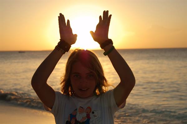 Girl on the beach raising hands against the low sun over the sea