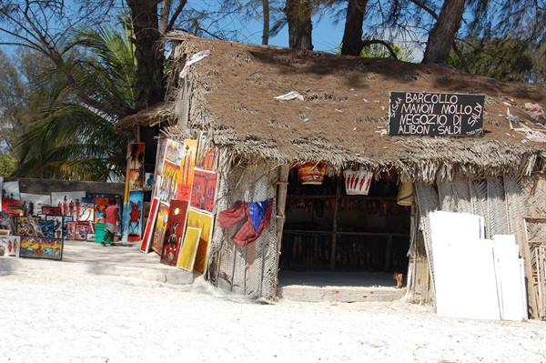 Thatched wooden stall on white sand, paintings for sale, boat taxi sign