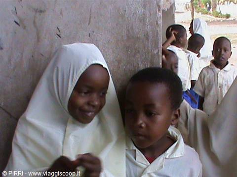 Smiling children in white uniforms next to a concrete wall