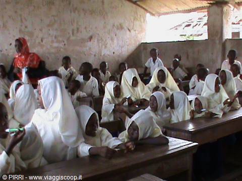 Girls in white headscarves sitting at wooden desks in a bare classroom