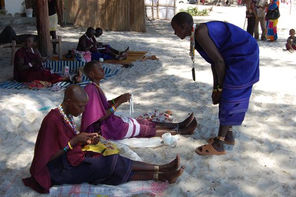 Maasai women in colorful robes making beaded jewelry on the sand