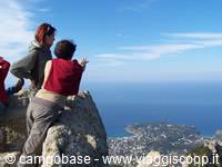 Tourists on granite rocks overlooking blue sea bay at Capo Testa