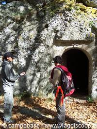 Two hikers standing before a cave entrance carved into rock in the woods