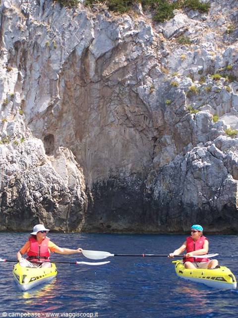Two women paddling yellow kayaks beneath white limestone cliffs