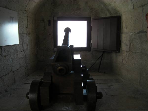 Dark wooden cannon aimed through a stone casemate window in Belém Tower