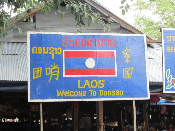 Blue sign with Laos flag in front of a wooden market in Donsao