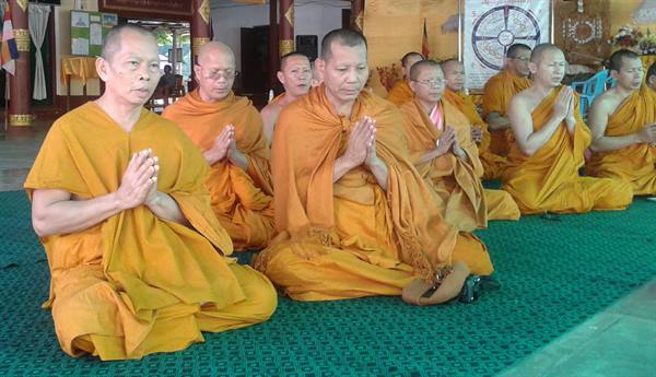 Buddhist monks in orange robes pray with joined hands inside a temple