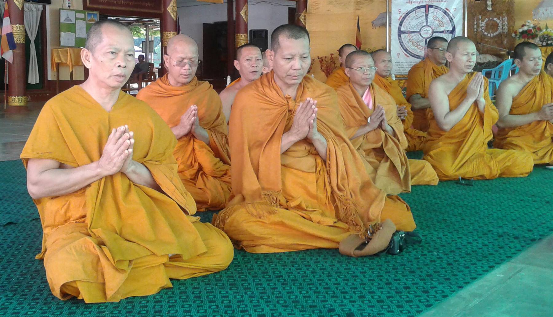 Buddhist monks in orange robes pray with joined hands inside a temple