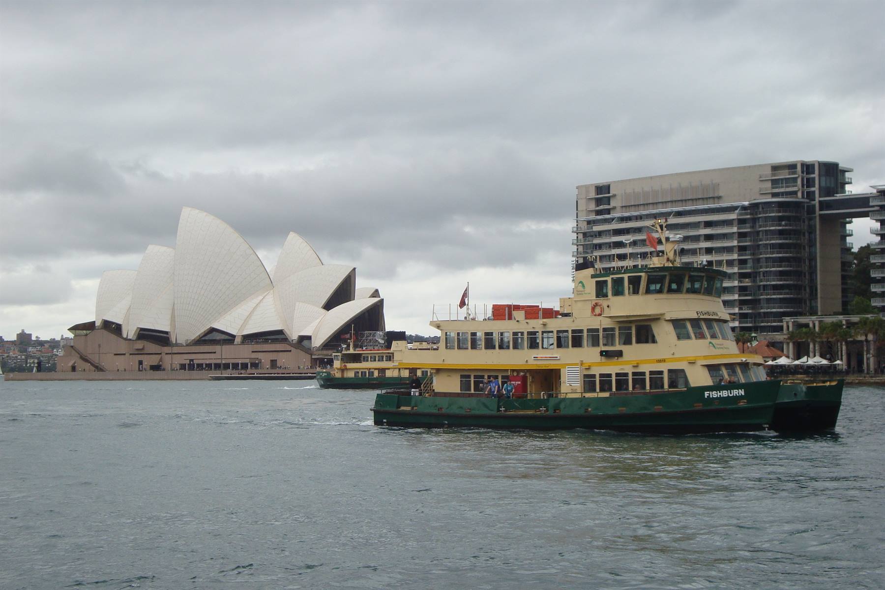 Green and yellow ferry near Sydney Opera House under overcast sky
