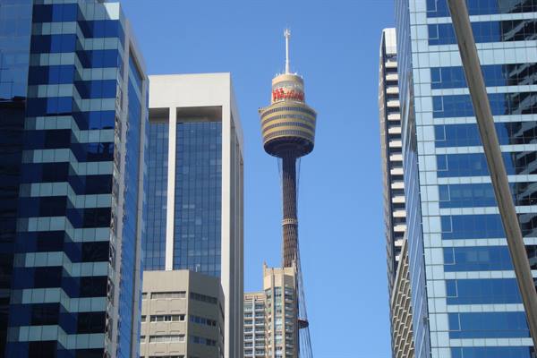 Sydney Tower rises among blue glass skyscrapers under a clear sky