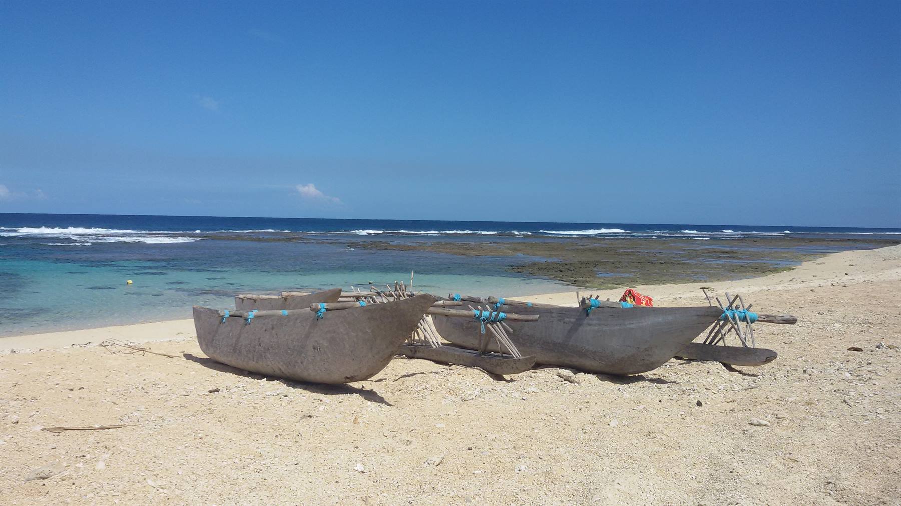 Wooden outrigger canoes resting on sandy beach in front of the reef