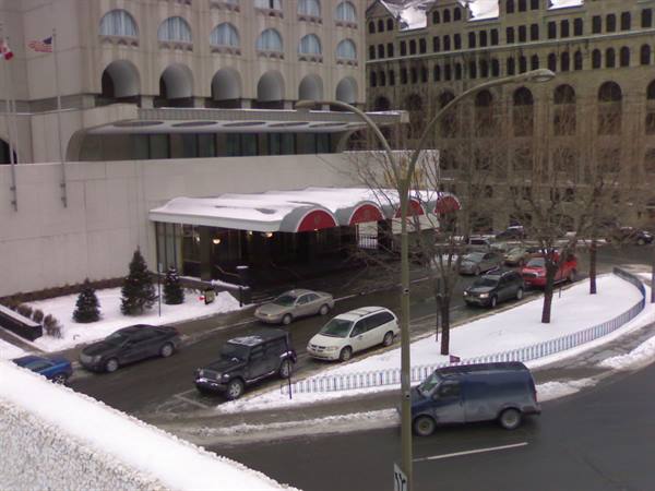 Cars waiting at a hotel entrance, snowy streets and bare winter trees