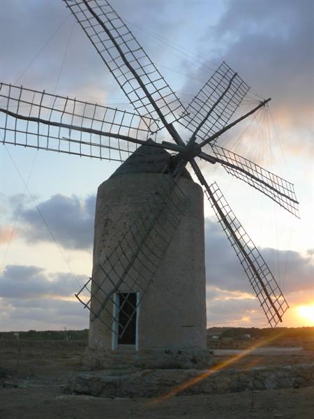 Old stone windmill with wooden lattice sails against cloudy sunset sky