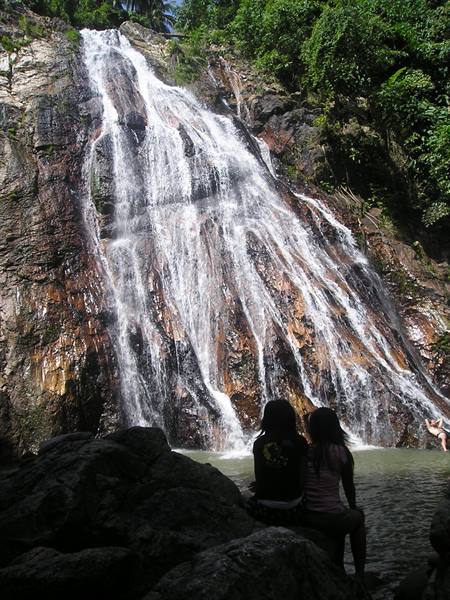 Two tourists sitting on rocks in front of Na Muang waterfall