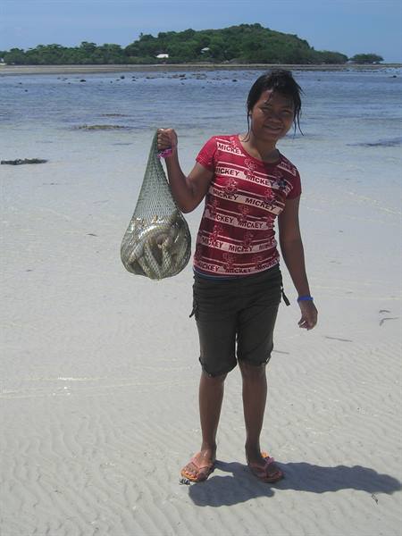 Girl on the beach showing a net full of freshly caught fish