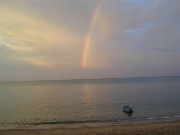 Rainbow over calm sea, small blue boat near the sandy beach