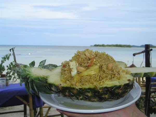 Fried rice served in a pineapple, beach and sea in the background