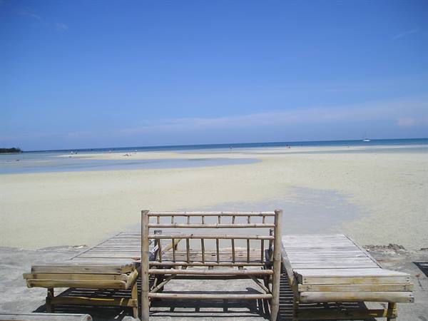 Empty bamboo chairs and table on white sand beach with shallow turquoise sea