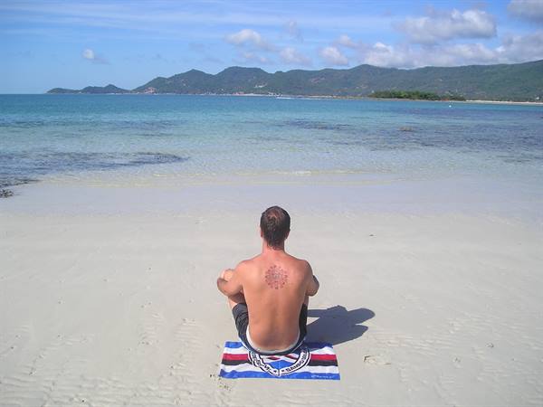 Man sitting cross-legged on a towel, white sand beach and turquoise sea