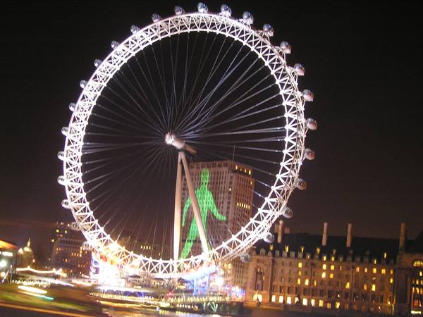 The London Eye lit white at night above Westminster buildings
