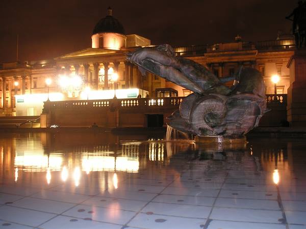 Bronze fountain at Trafalgar Square by night, illuminated National Gallery, water reflections
