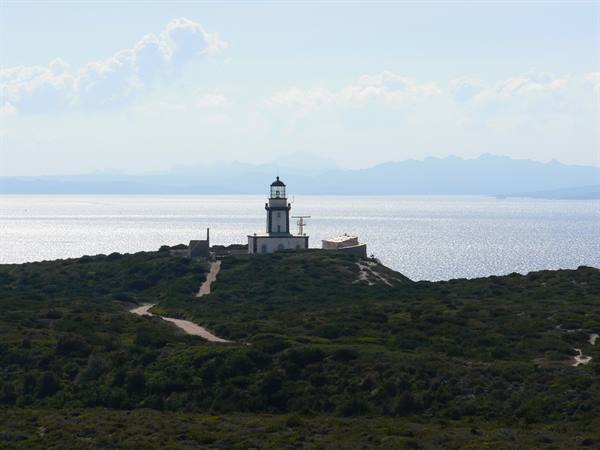 White lighthouse on green hill, dirt paths, sparkling sea and distant mountains