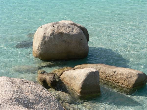 Granite boulders in clear turquoise water under bright sunlight