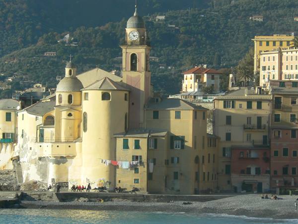 Yellow basilica with clock bell tower overlooking the pebble beach in Camogli